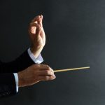Music_conductor_hands_with_baton_on_black_background