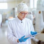Supervisor_in_sterile_uniform_and_with_eyeglasses_using_tablet_for_controlling_workflow_in_food_factory.;_Shutterstock_ID_1425383438;_purchase_order:_TAG1-CJ-04;_job:_TAG1_CJ;_client:_TÜV_SÜD;_other:_