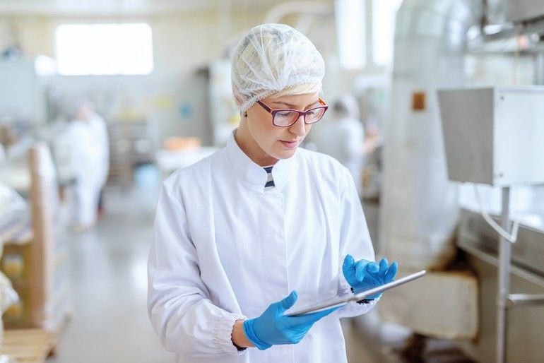 Supervisor_in_sterile_uniform_and_with_eyeglasses_using_tablet_for_controlling_workflow_in_food_factory.;_Shutterstock_ID_1425383438;_purchase_order:_TAG1-CJ-04;_job:_TAG1_CJ;_client:_TÜV_SÜD;_other:_