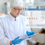 Supervisor_in_sterile_uniform_and_with_eyeglasses_using_tablet_for_controlling_workflow_in_food_factory.